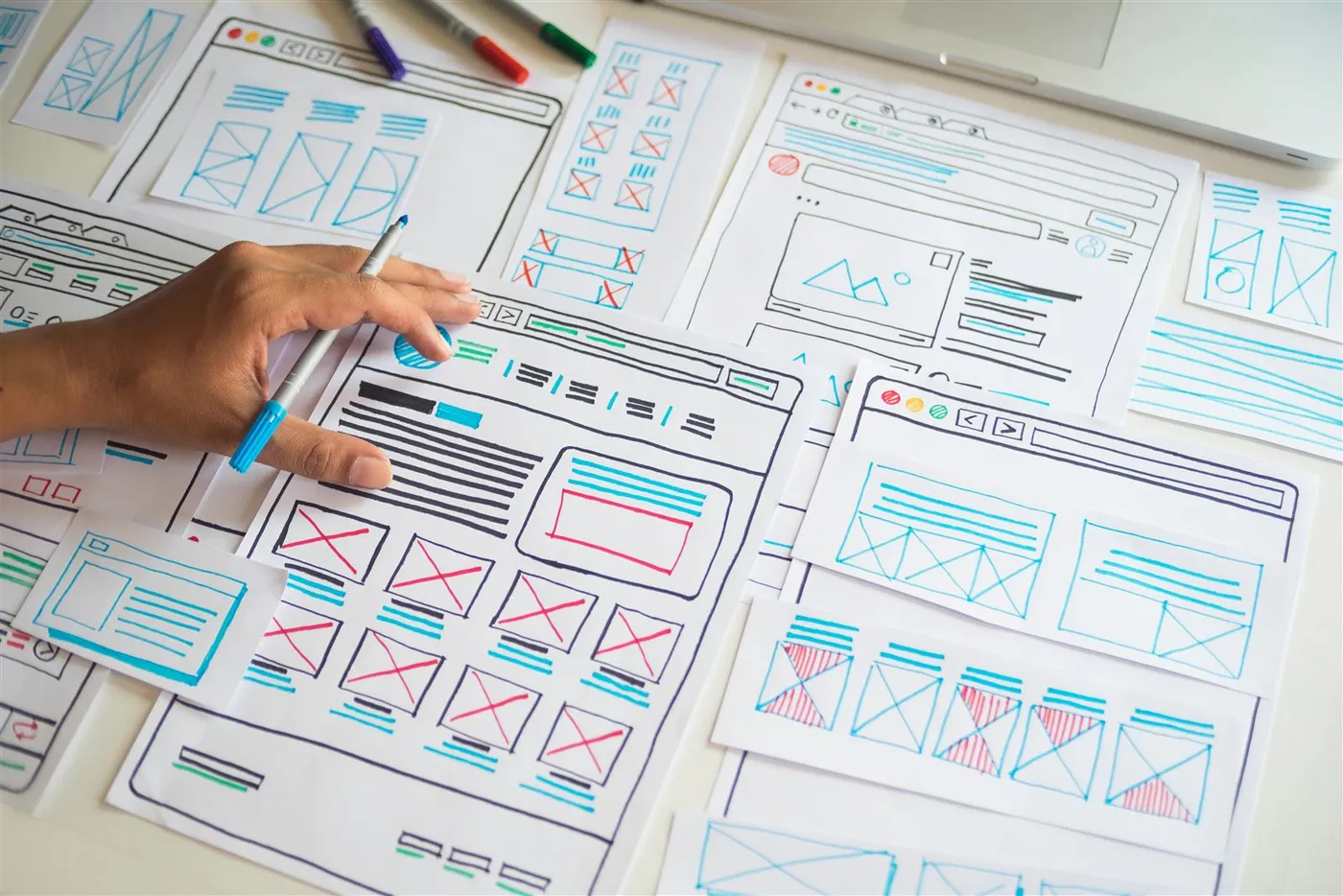 A designer's hand working through paper wireframe sketches of website layouts
